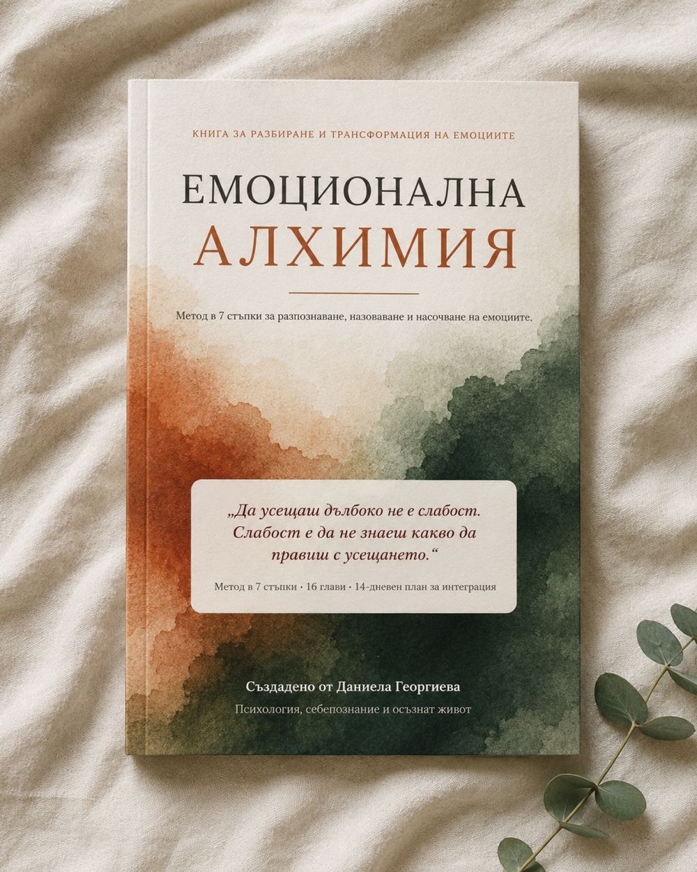 Книгата Емоционална Алхимия върху светъл текстилен фон